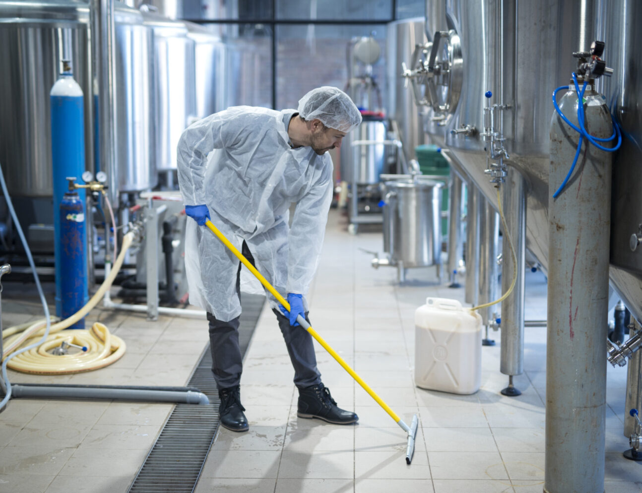 Professional industrial cleaner in protective uniform cleaning floor of food processing plant.